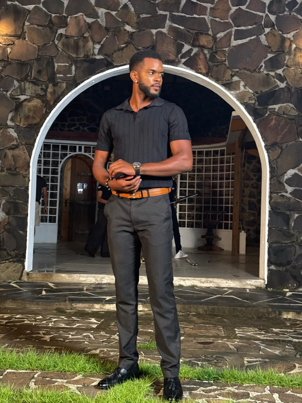 Derrick en polo noir devant une arche en pierre